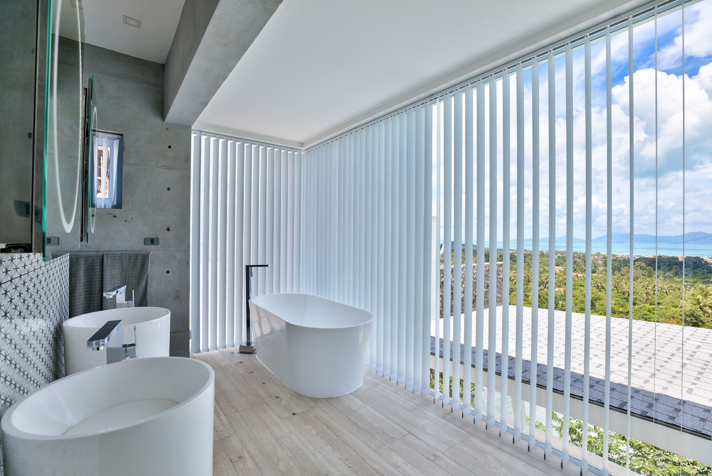 Ein modernes Badezimmer mit einer großen Badewanne, einem Waschbecken und einem Spiegel. Es verfügt über ein großes Fenster mit Blick ins Freie.