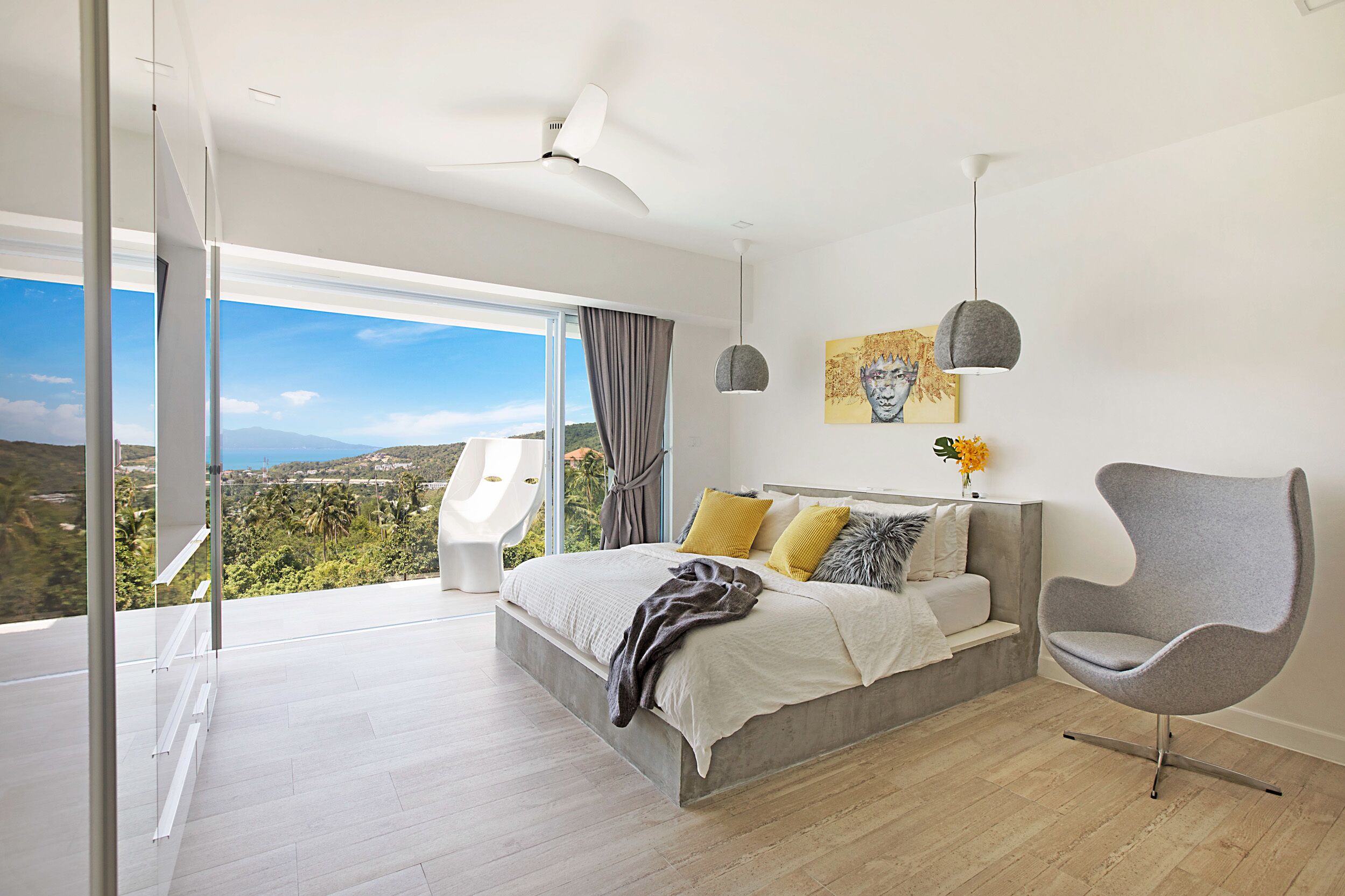 Un dormitorio moderno con una cama grande, un sillón gris y vistas al paisaje a través de amplios ventanales.