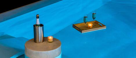 A blue-lit pool area with a champagne bottle, candle, and a tray with glasses.