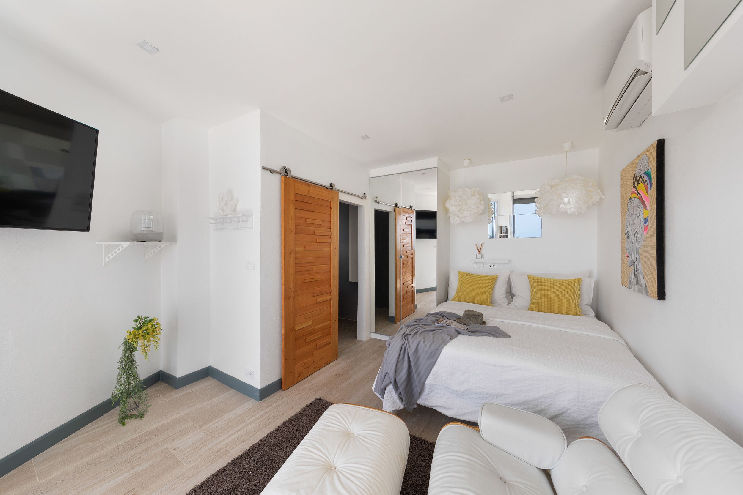 Quarto moderno com cama, televisão, espelho e porta que dá para outro espaço.