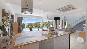 Une cuisine moderne dotée d’un grand îlot central, d’un coin repas offrant une vue agréable et d’un escalier menant à un balcon.