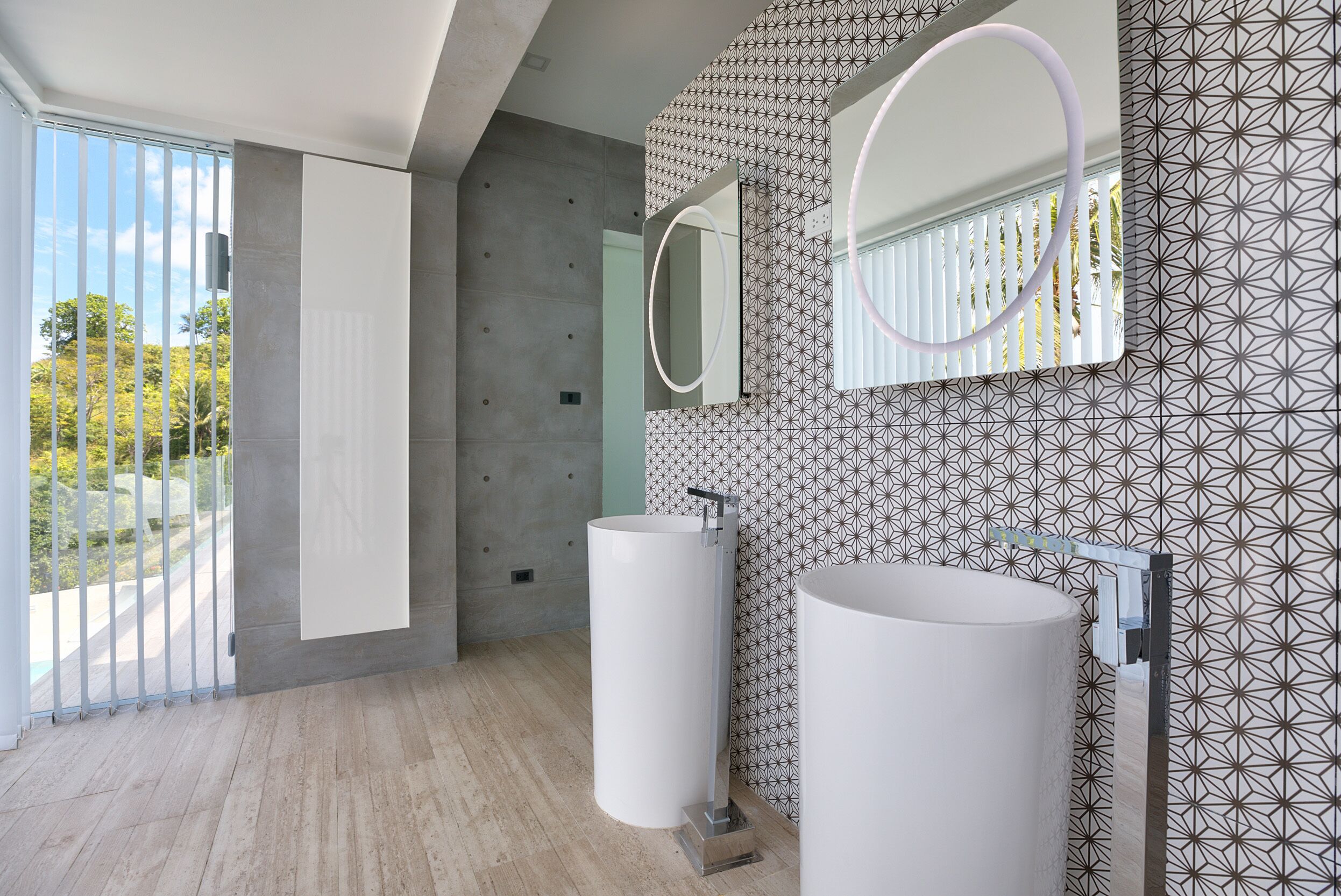 A modern bathroom with two large white sinks, a mirror with a circular light, and a patterned wall.