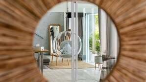Un salon moderne avec un miroir rond, un fauteuil rond, une table en verre et une vue sur l’extérieur.