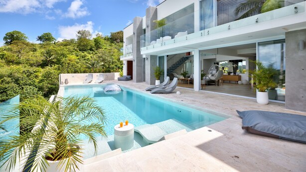 Une maison moderne dotée d’une piscine, de balustrades en verre et d’un espace salon extérieur.