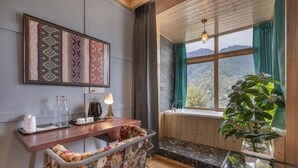 A cozy room with a wooden ceiling, a large window with a view of mountains, a wooden bench, a small table with a lamp, and a potted plant. - Echor Himalayan Heights Luxe Resort & Spa, Manali (Manali)