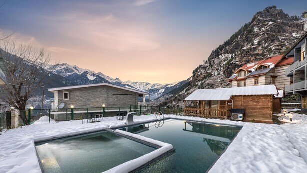 A snow-covered outdoor pool area with a mountain backdrop, wooden buildings, and a stone house. - Echor Himalayan Heights Luxe Resort & Spa, Manali (Manali)