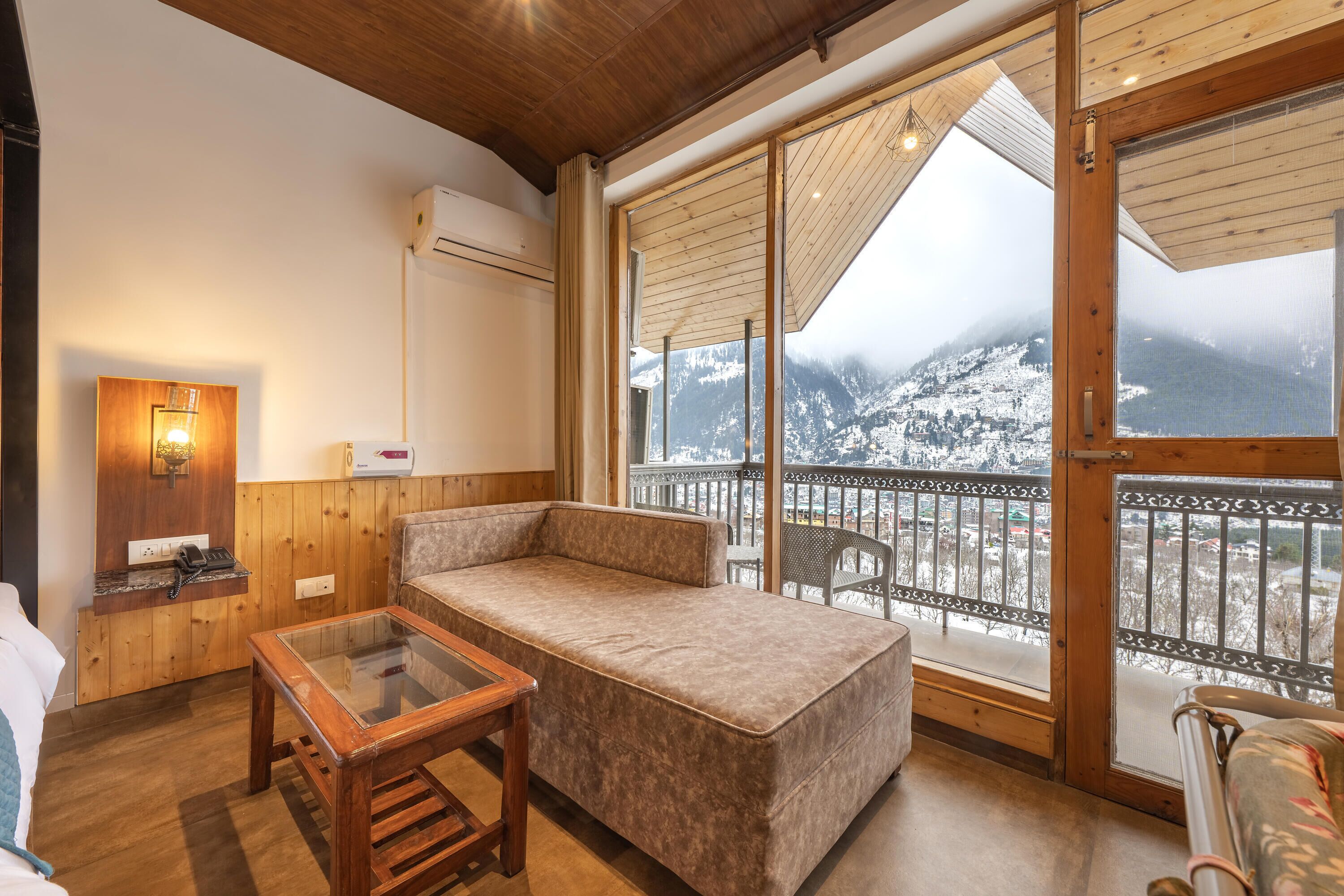 Ein gemütliches Zimmer mit einer Couch, einem Glastisch und Blick auf verschneite Berge durch große Fenster.