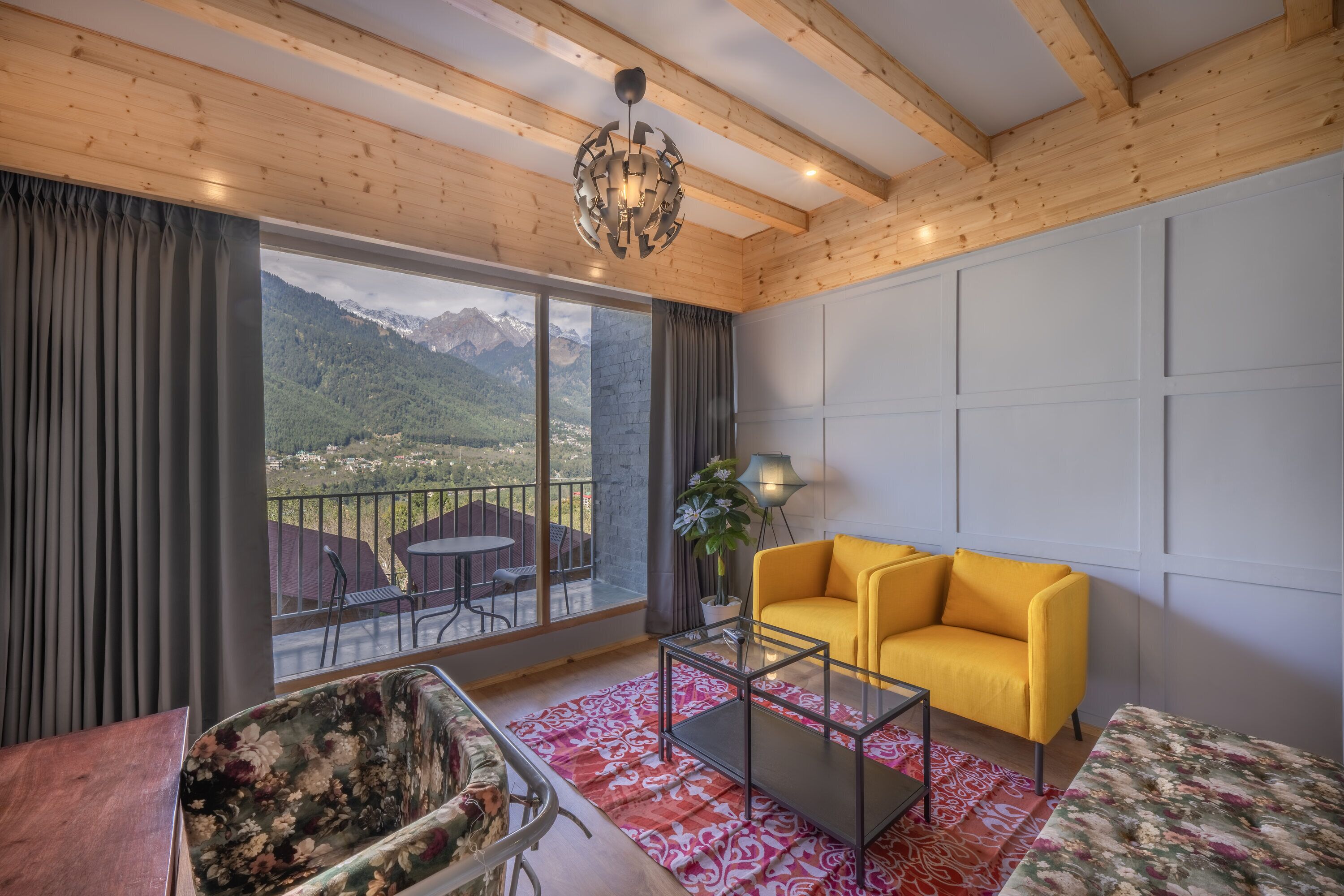 A modern living room with a yellow sofa, a glass coffee table, and a view of mountains through large windows.