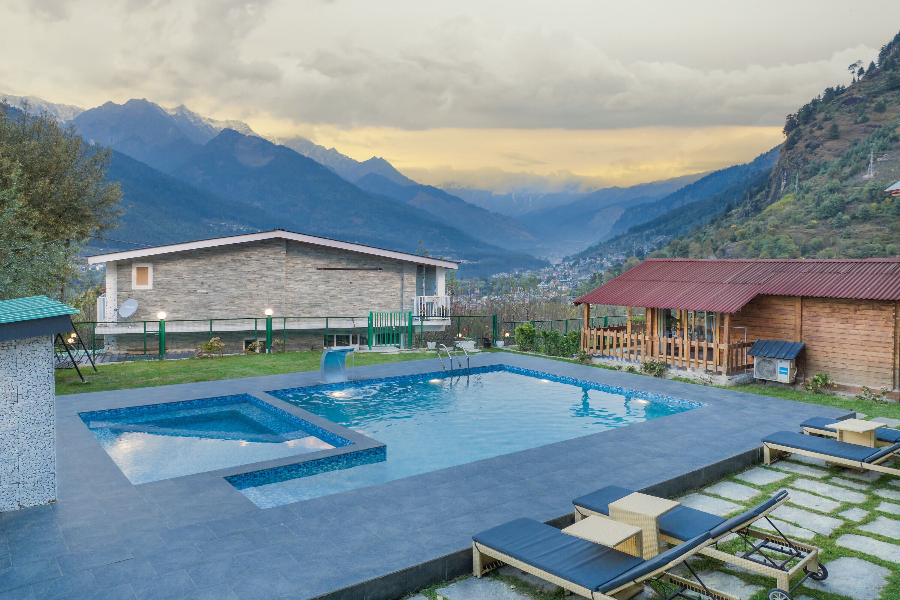 A pool area with lounge chairs, a stone building, and a view of mountains.