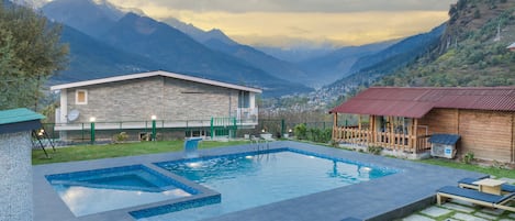 A pool area with lounge chairs, a stone building, and a view of mountains.
