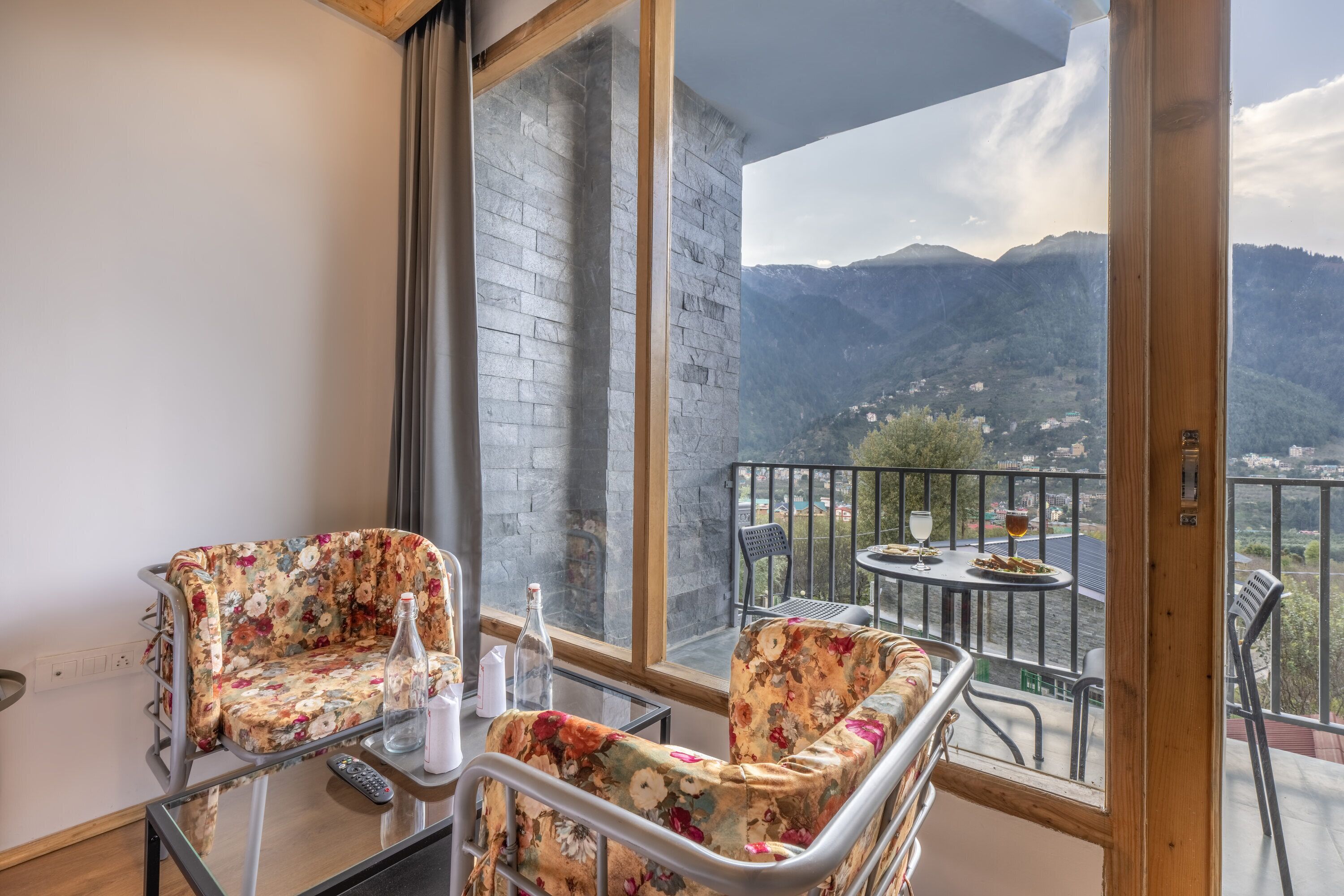 A balcony with two floral chairs, a small table, and a bottle.