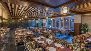 A spacious indoor dining area with multiple tables and chairs, a stone wall, and large windows. - Echor Himalayan Heights Luxe Resort & Spa, Manali (Manali)