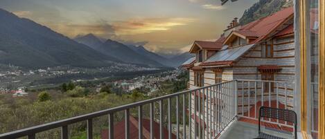 A balcony with a metal railing overlooking a mountainous landscape and a town below.