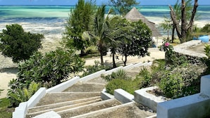 Une vue sur la plage avec une cabane à toit de chaume, des palmiers et un escalier menant à la plage.