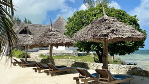 Une plage avec des parasols en chaume et des chaises longues en bois.