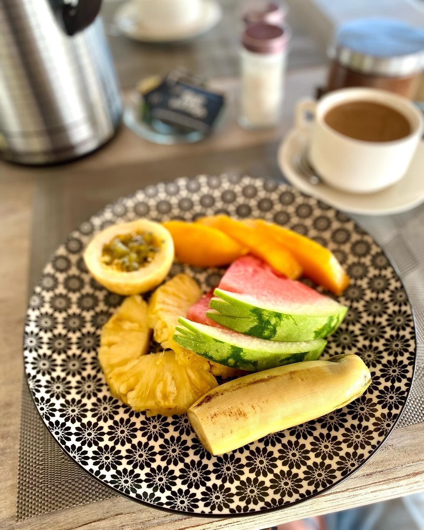 A plate with pineapple, watermelon, and orange slices on a patterned tablecloth.