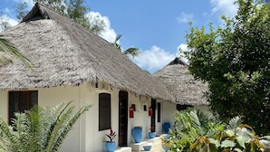 Un bungalow avec un toit de chaume, un chemin de terre et des plantes en pot.