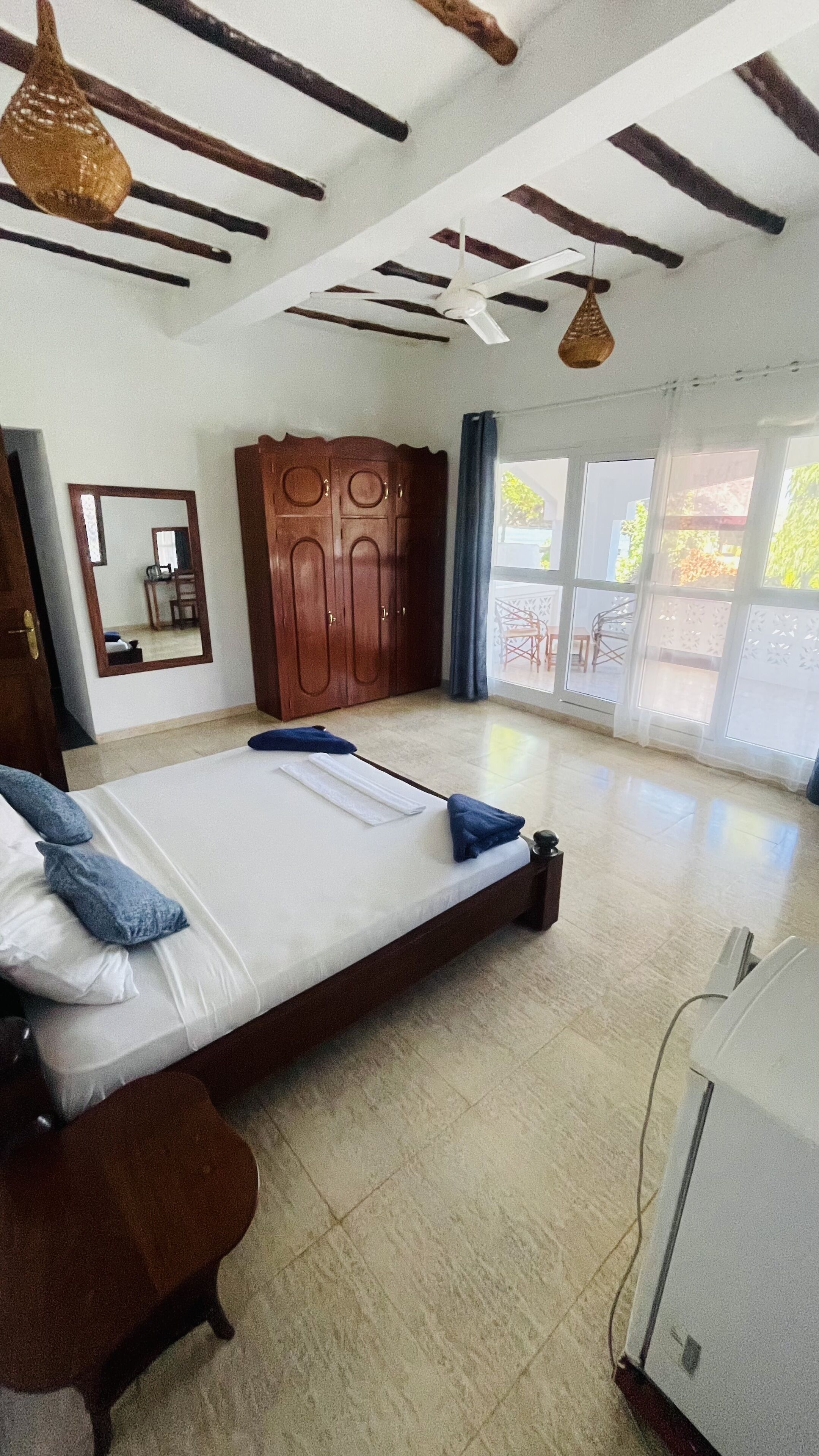 A spacious room with a large bed, wooden wardrobe, and a ceiling fan.