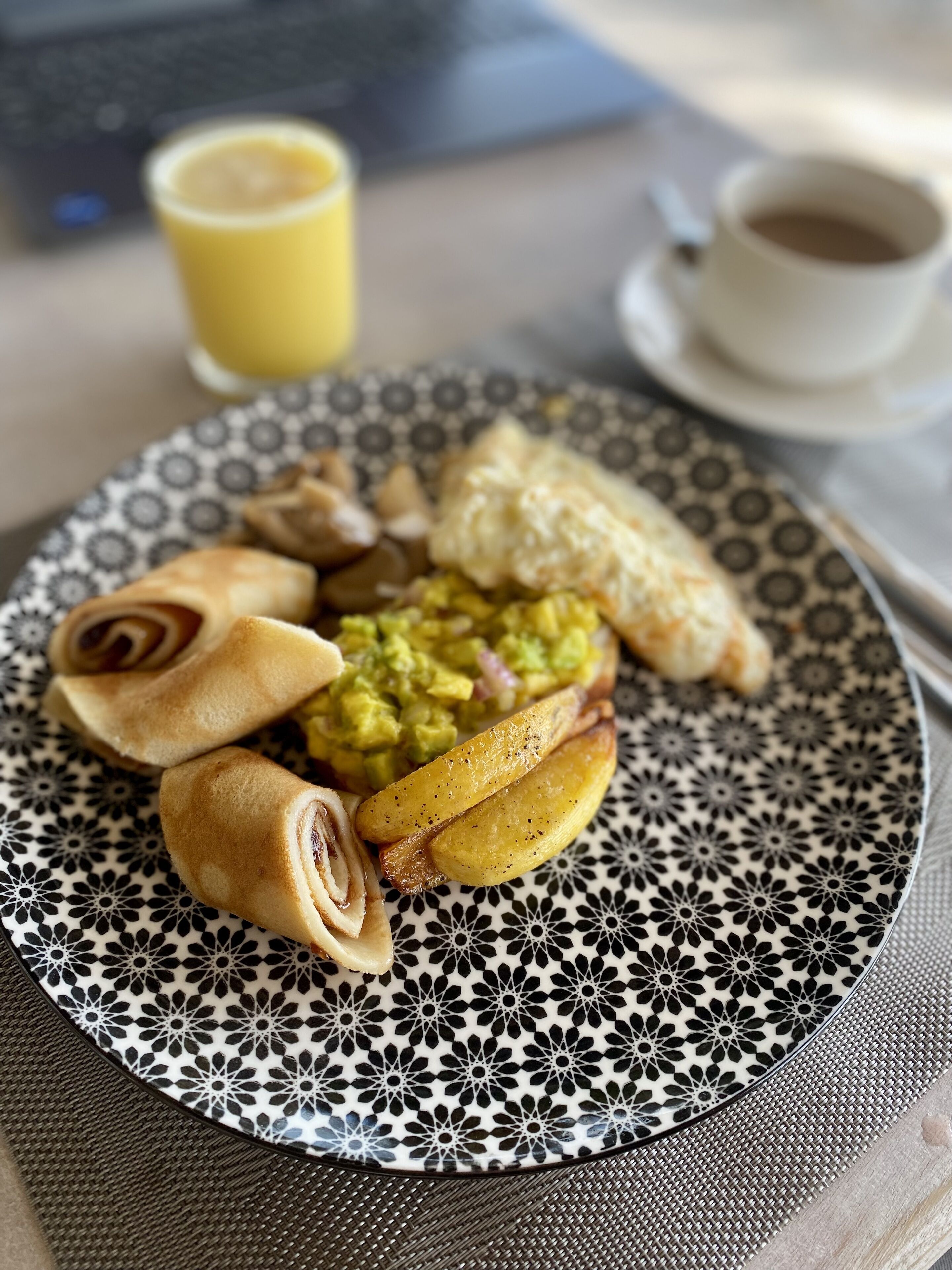 Ein Teller mit Speisen, darunter Pfannkuchen, Kartoffeln und ein grüner Aufstrich, dazu eine Tasse Kaffee und ein Glas Orangensaft.