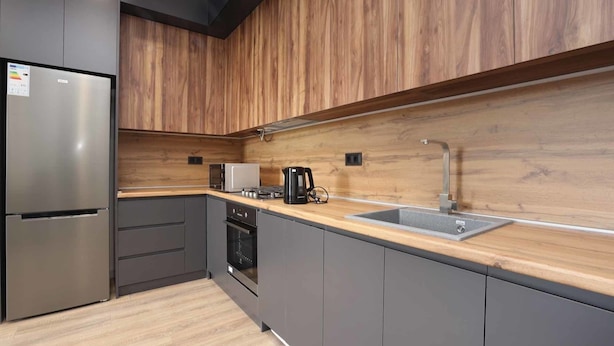 Een moderne keuken met houten kastjes, een roestvrijstalen koelkast, een magnetron, een koffiezetapparaat en een gootsteen.