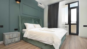 Een moderne slaapkamer met een groot bed, een nachtkastje, een luchtverkoeler aan de muur en uitzicht op de omgeving via een schuifdeur.
