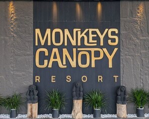 Señalización para 'MONKEYS CANOPY RESORT' con una pared texturizada y estatuas decorativas.