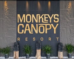 Señalización para 'MONKEYS CANOPY RESORT' con una pared texturizada y estatuas decorativas.