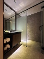 Un baño moderno con cabina de ducha de vidrio, tocador de madera con espejo y repisa con toallas.