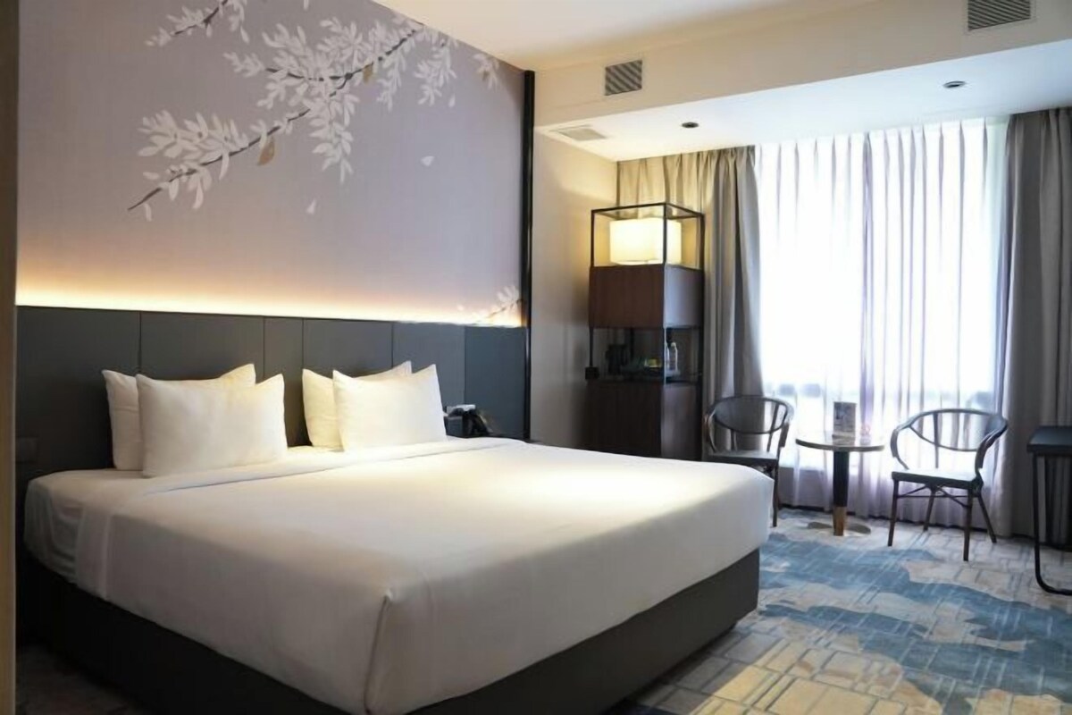 A hotel room with a large bed, a desk, a chair, and a lamp.
