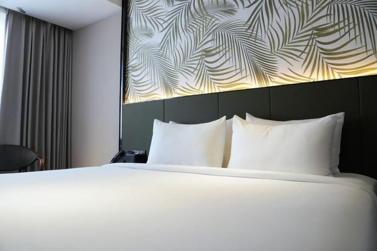 A hotel room with a large bed, a headboard with a leaf pattern, a chair, and a nightstand.