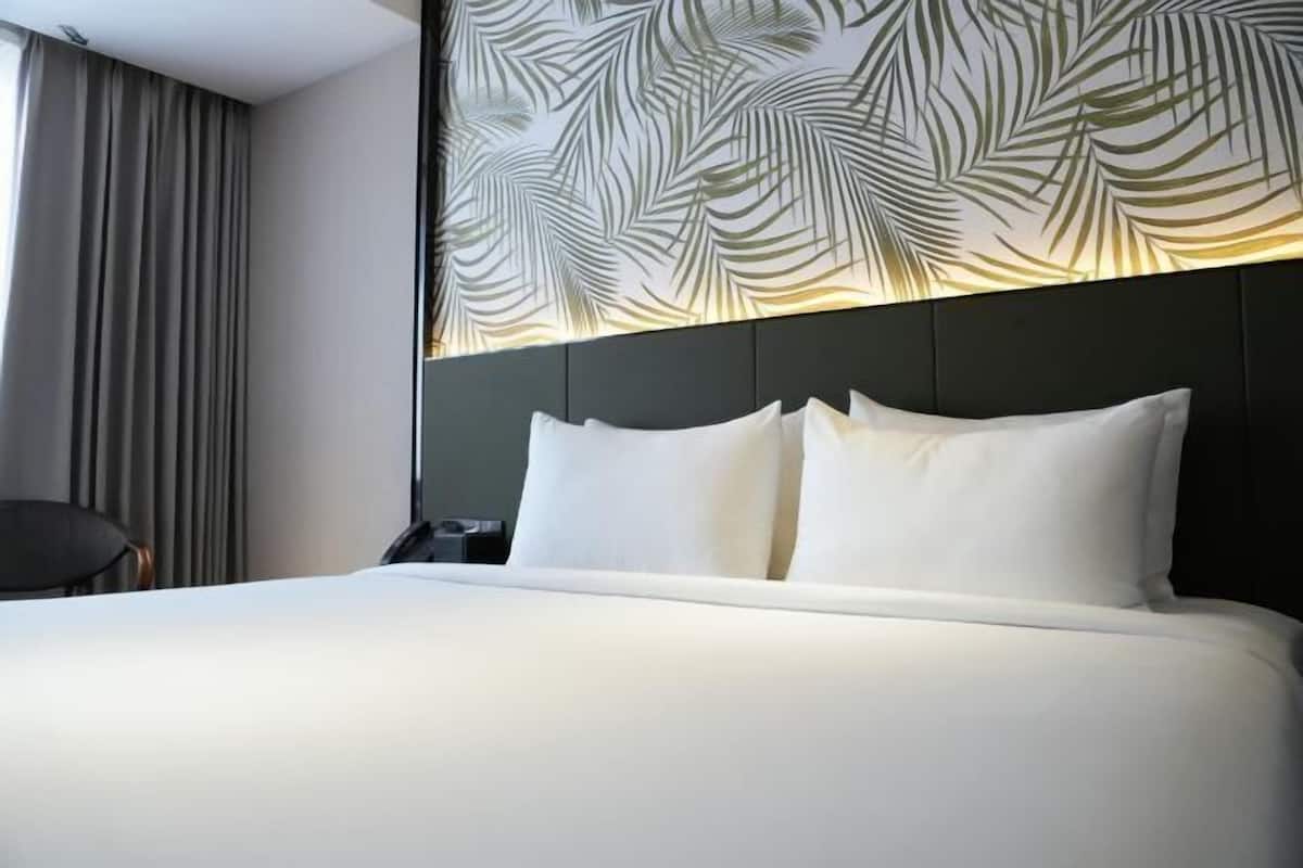 A hotel room with a large bed, a headboard with a leaf pattern, a chair, and a nightstand.