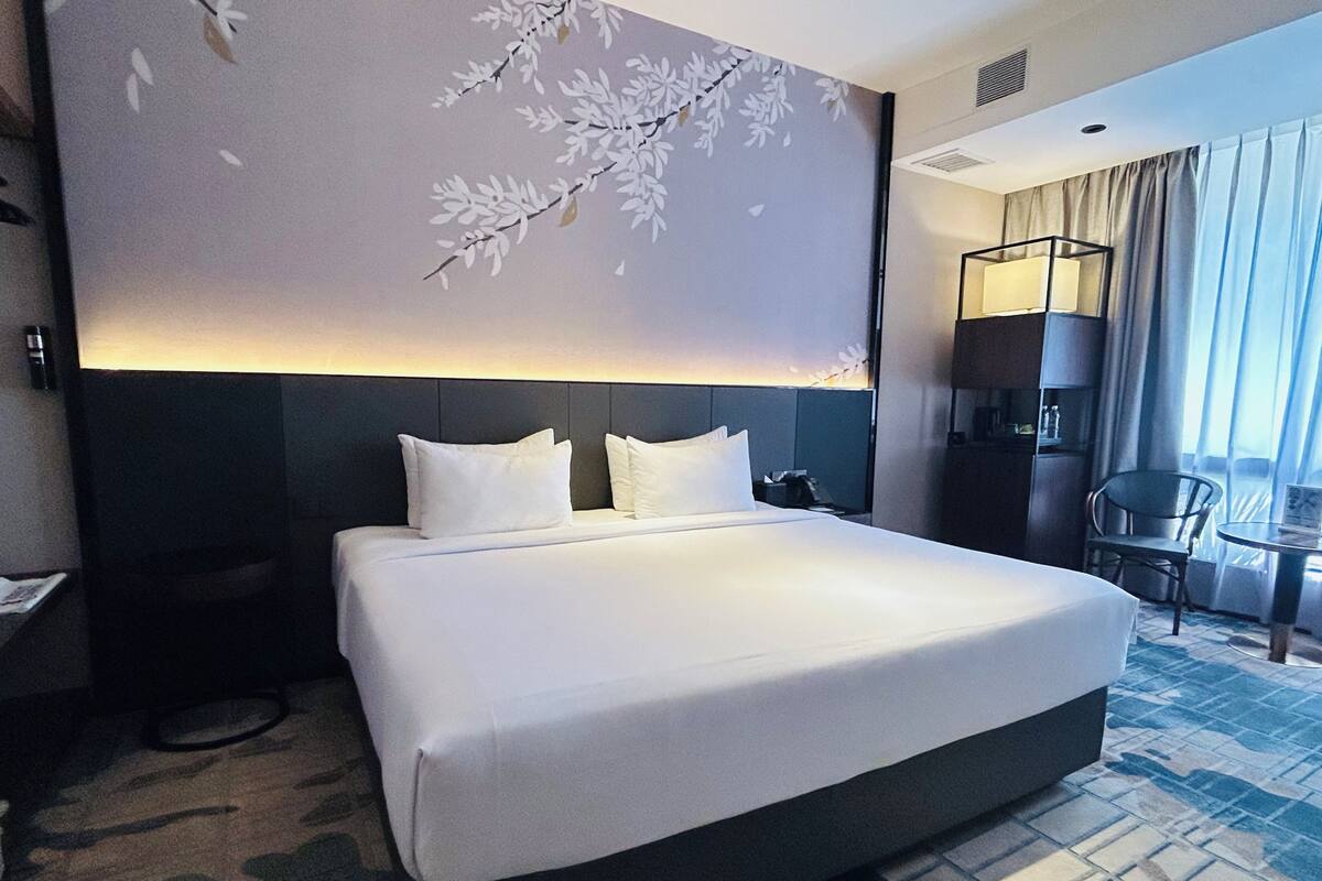 A hotel room with a large bed, a desk, a chair, a lamp, and a view of the outdoors.
