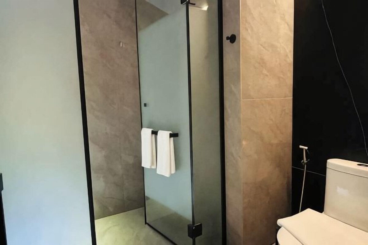 A modern bathroom with a glass shower enclosure, a toilet, and a mirror reflecting a towel rack.