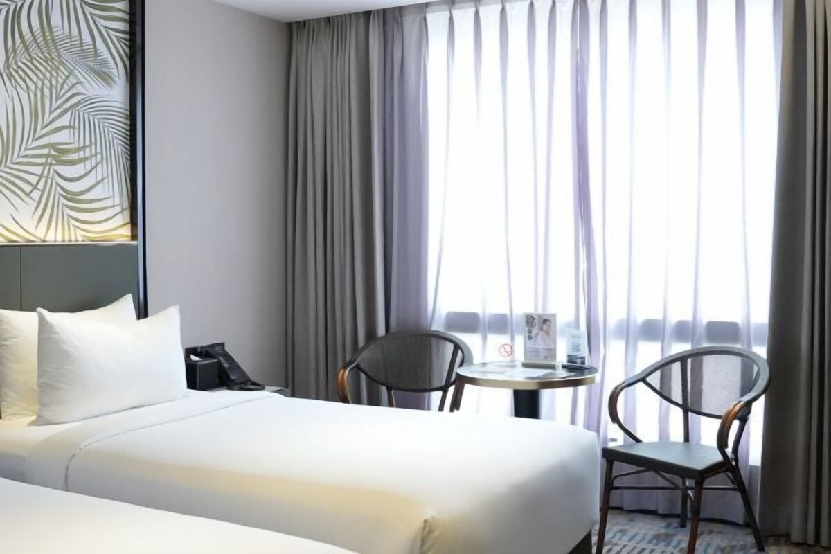 Una habitación de hotel con una cama, una silla, una mesita y un ventanal con cortinas.