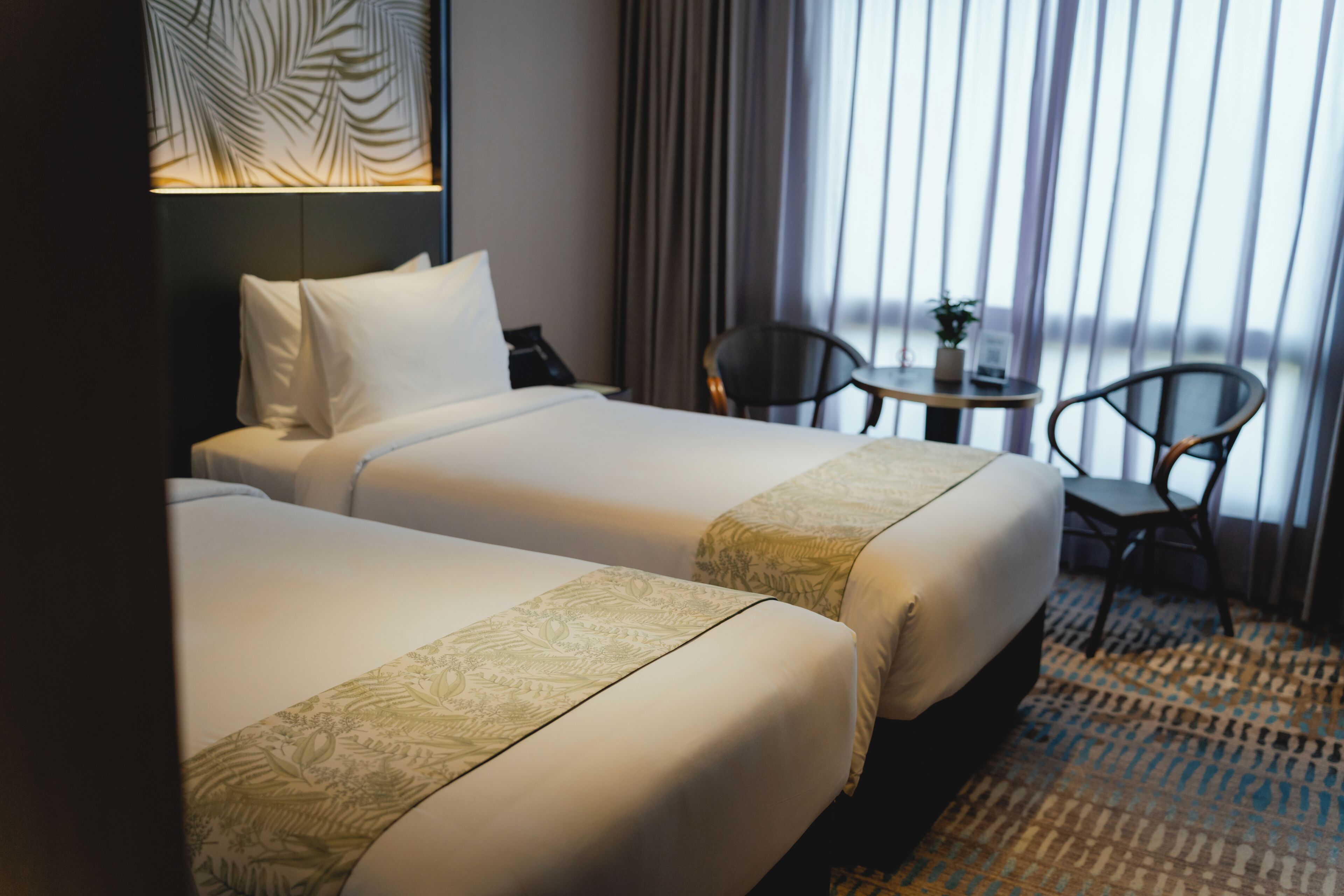 Une chambre d’hôtel avec deux lits, une petite table, des chaises, une lampe et une vue sur l’extérieur.