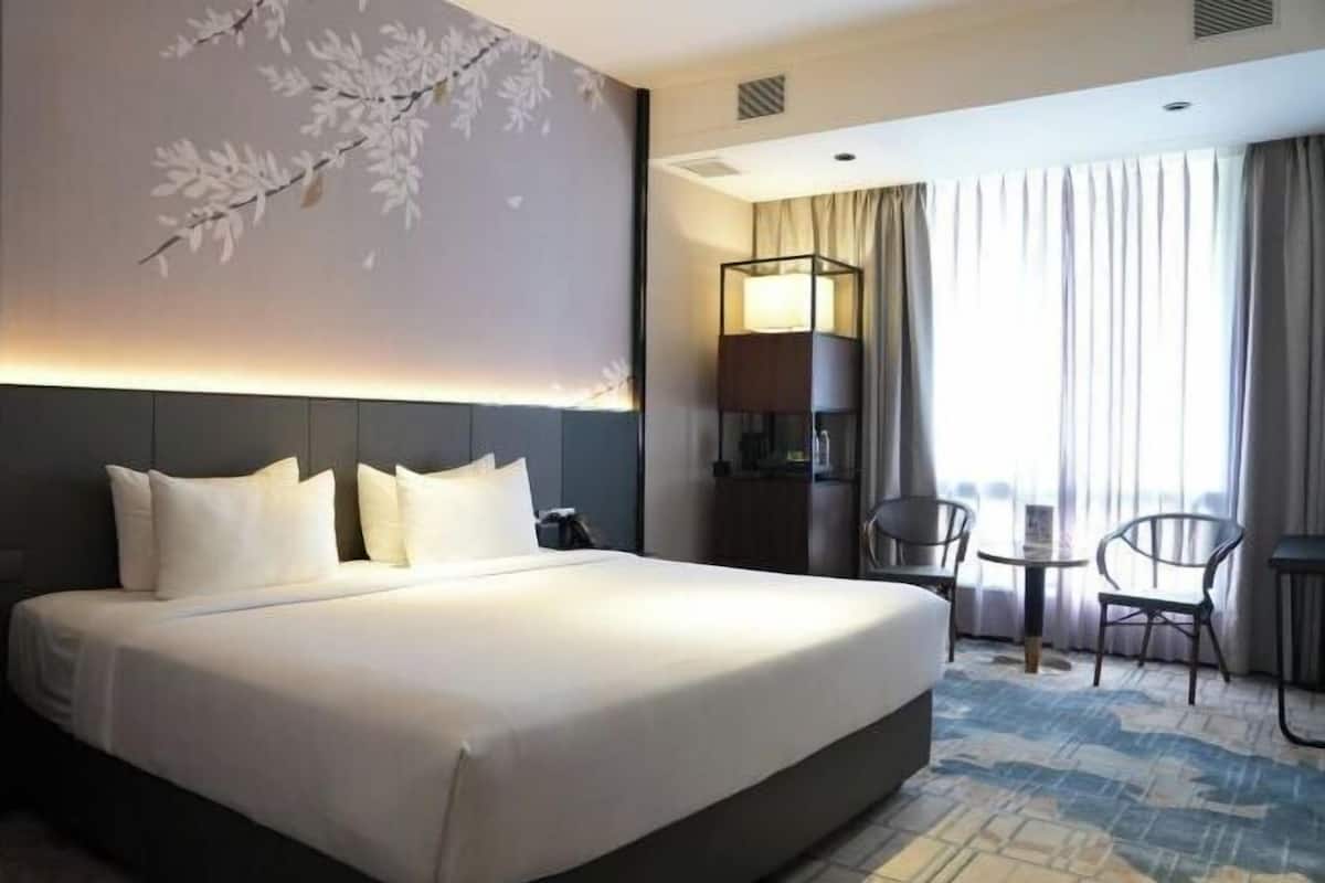 A hotel room with a large bed, a desk with a lamp, a chair, and a view of the outdoors.