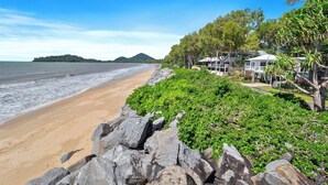 A beach with a rocky foreground, a sandy shore, and a row of houses with a view of the sea. - Seaside Rest at Clifton Beach (Clifton Beach)