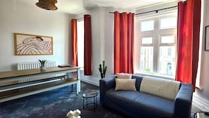 A living room with a sofa, a coffee table, a radiator, a cactus, and a window with curtains. - Claude Road Apartments by Switchback Stays (Cardiff)