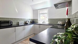 A kitchen with white cabinets, a black countertop, a microwave, a kettle, and a window. - Claude Road Apartments by Switchback Stays (Cardiff)