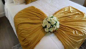 Ein Bett mit einer großen, goldenen, gefältelten Tagesdecke und einem Strauß weißer Blumen in der Mitte.