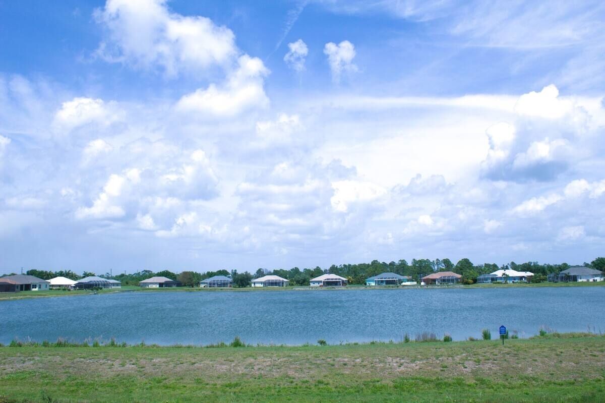 A lakeside view with several buildings, including a large white structure and smaller houses, under a partly cloudy sky.