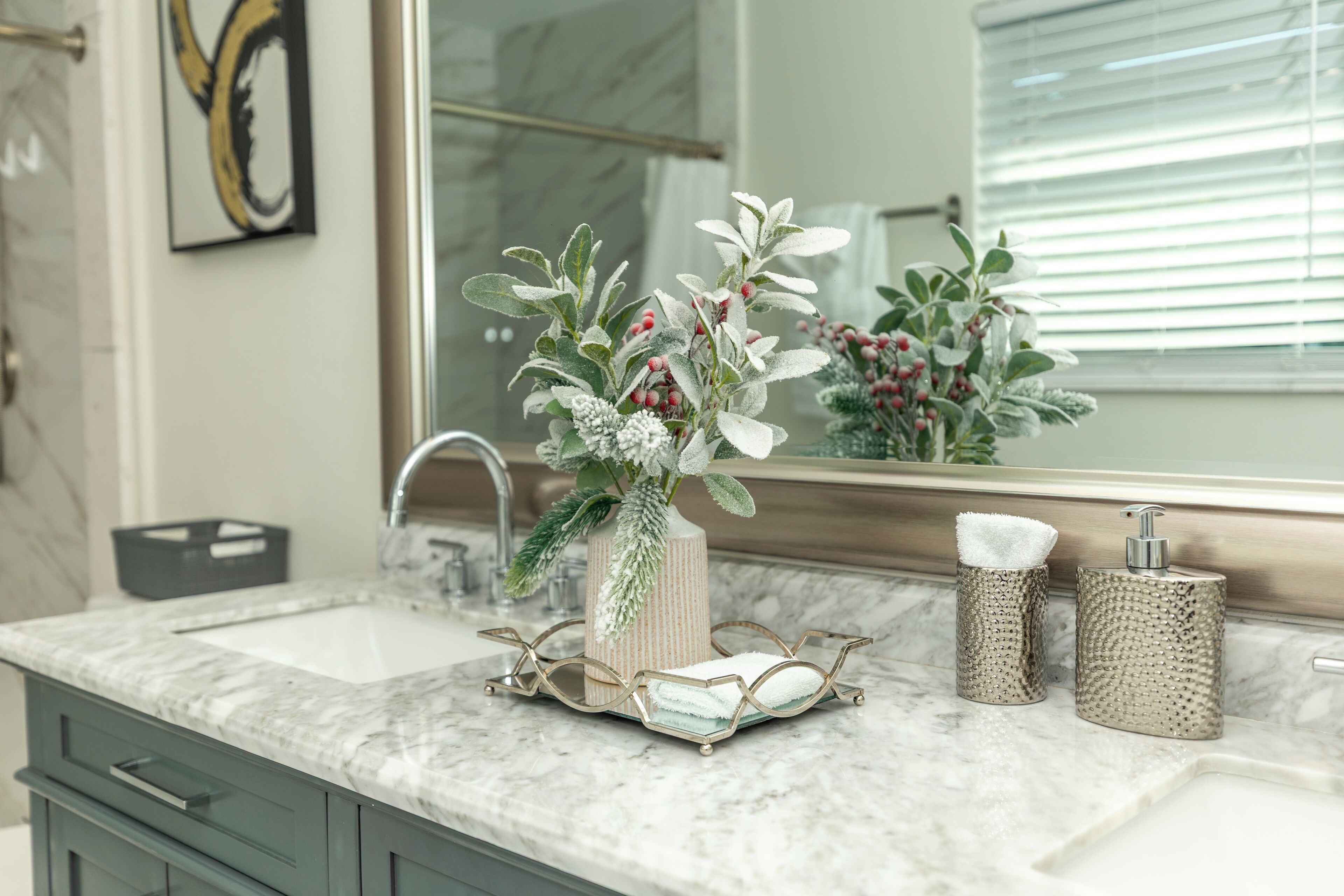 A bathroom with a marble sink, a mirror, a vase with greenery, and two soap dispensers.