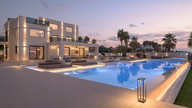 Una casa moderna de varios pisos con piscina, mobiliario exterior y palmeras.