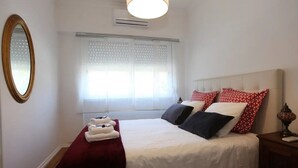 A hotel room with a bed, a bedside table, a mirror, and a window with blinds. - Private Terrace with Sun 15 minutes from Lisbon and the Airport (Odivelas)