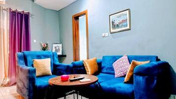 Un salon avec un canapé bleu, une table basse ronde et un tableau accroché au mur.