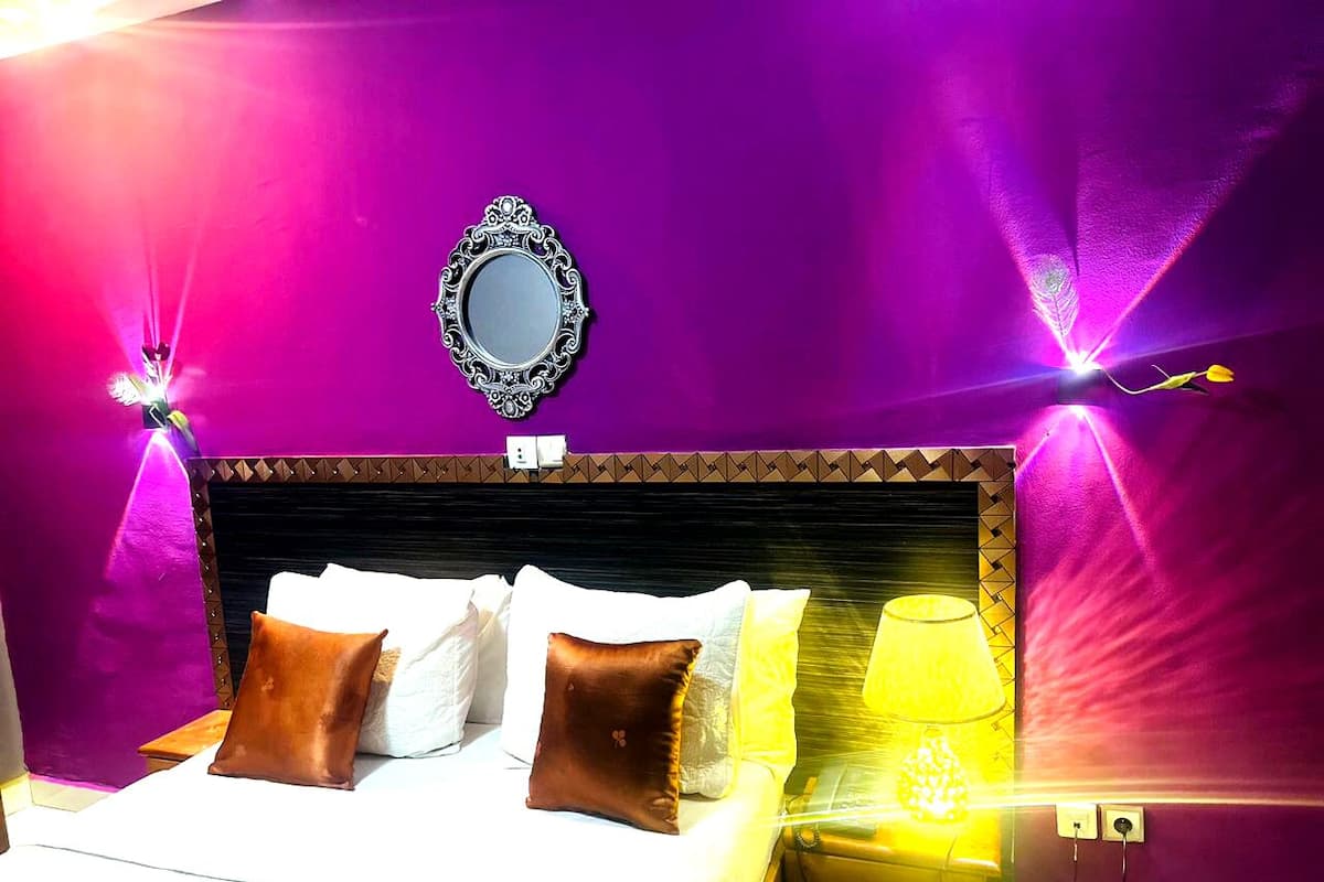 A bed with white and brown pillows, a mirror above it, and a lamp on the nightstand.