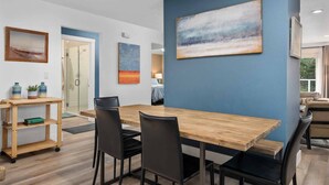 Un comedor moderno con una mesa de madera y sillas negras, una pared azul de acento y un cuadro.