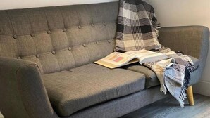 A grey sofa with a plaid blanket and a book on it. - Immaculate 1-bed Apartment in Sheffield (Sheffield)