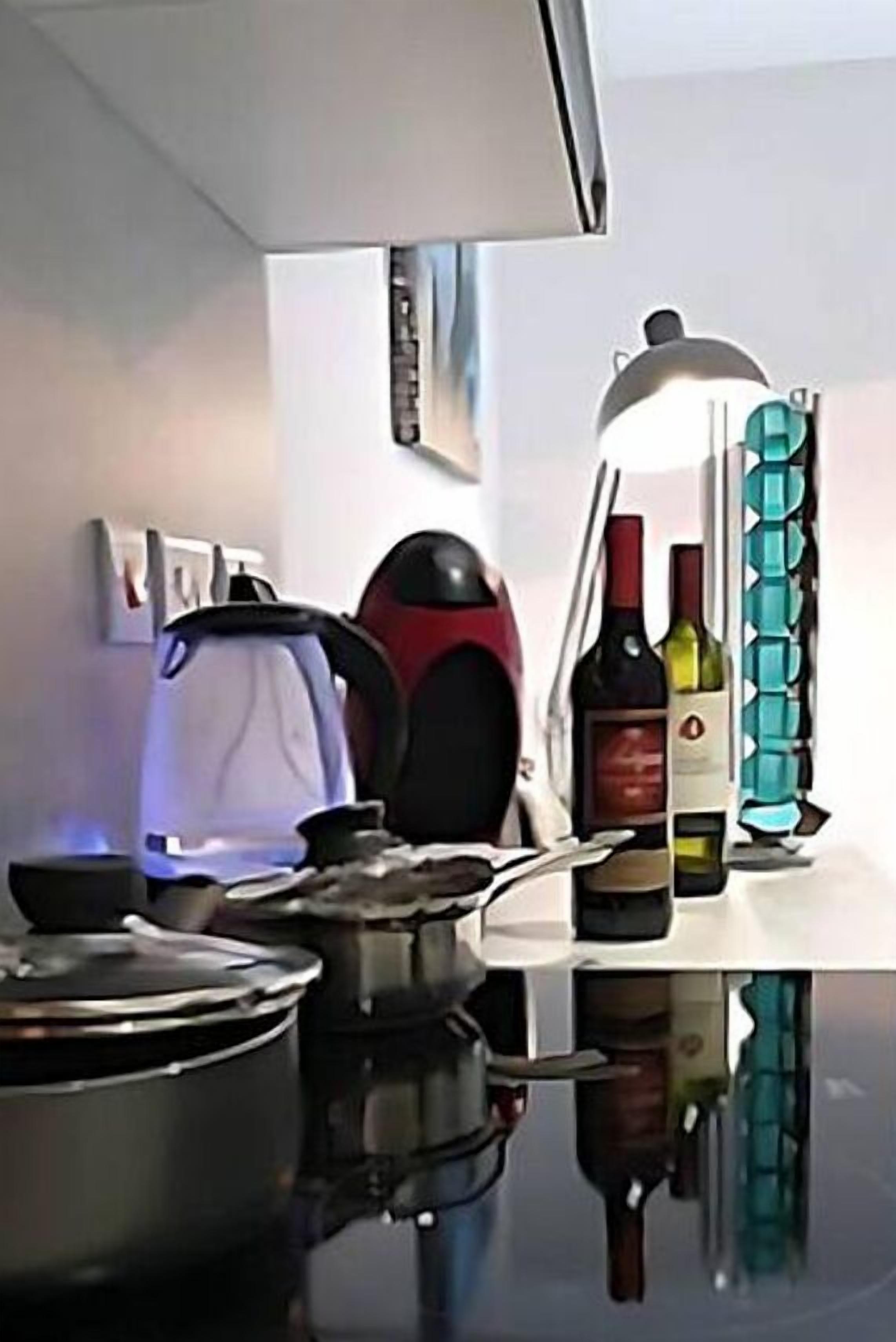 A kitchen with a stove, pots, a kettle, a coffee maker, and a wine rack with bottles.