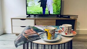 A television displaying a scene with two people walking outdoors, a table with a coffee mug and saucer, and a magazine on the table. - Immaculate 1-bed Apartment in Sheffield (Sheffield)